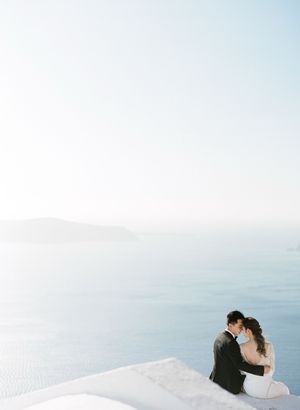 Couple sharing a romantic embrace on a white terrace overlooking the stunning blue Aegean Sea in Santorini.