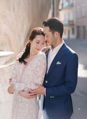 Couple sharing a tender embrace against a sunlit stone wall in a charming European town.
