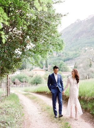 Couple walking hand in hand along a rustic dirt path through a scenic Italian countryside valley.