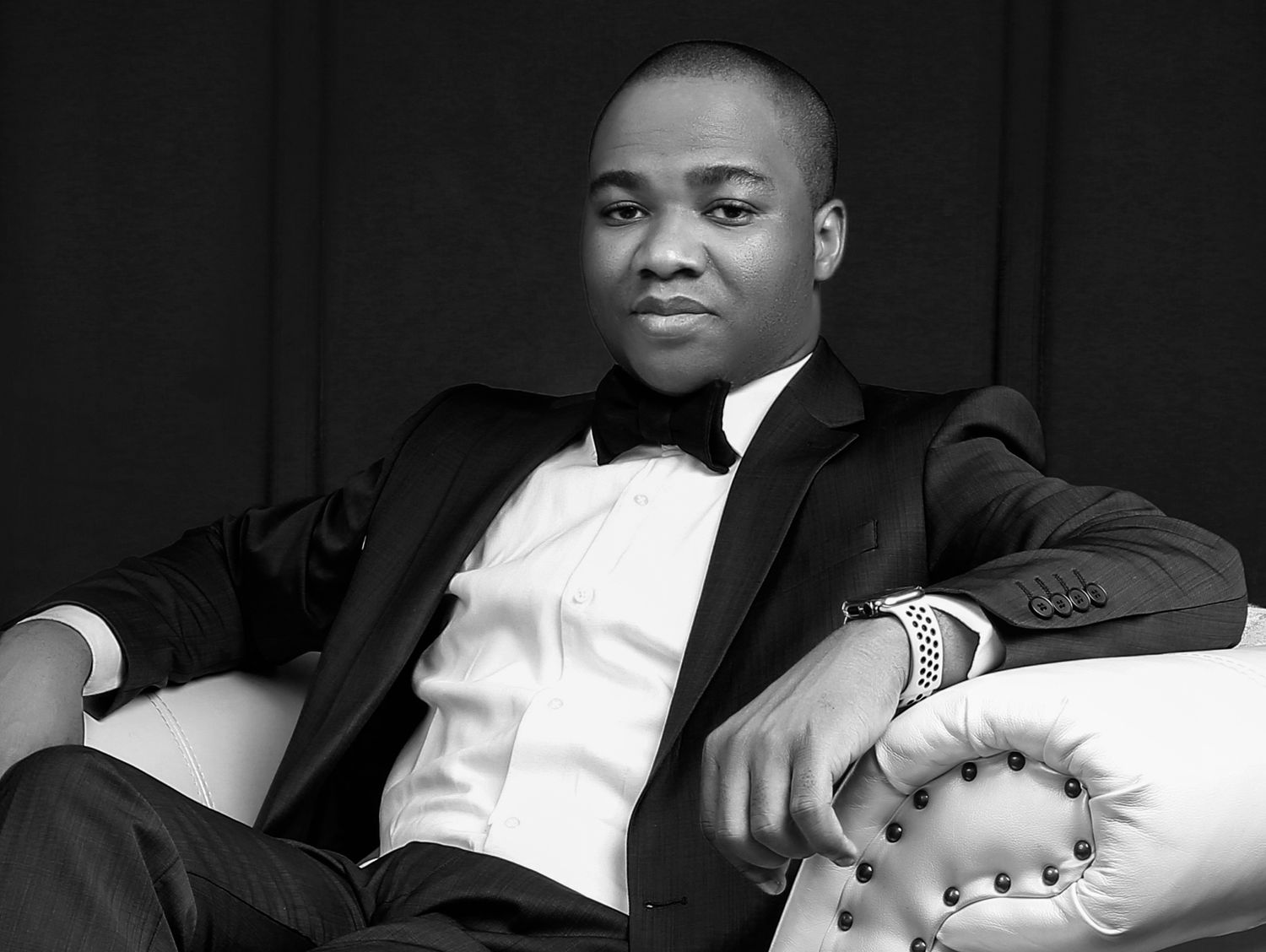 Elegant portrait of gentleman in white tuxedo jacket and bow tie against dark background.
