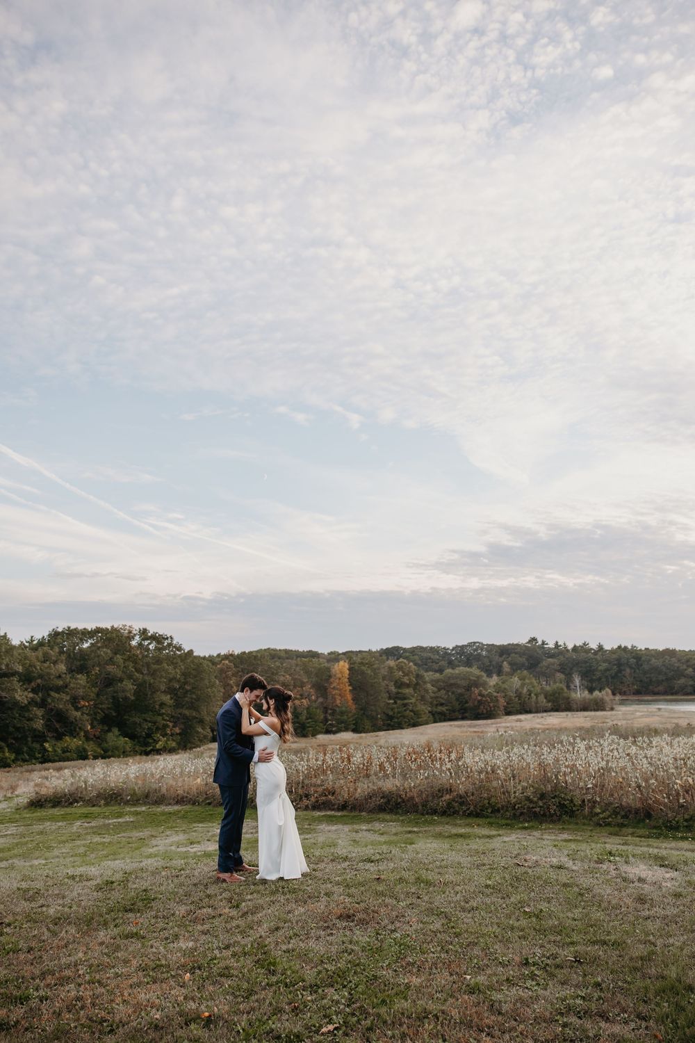 A wide landscape wedding photo with a couple standing in a distant field at sunset.
