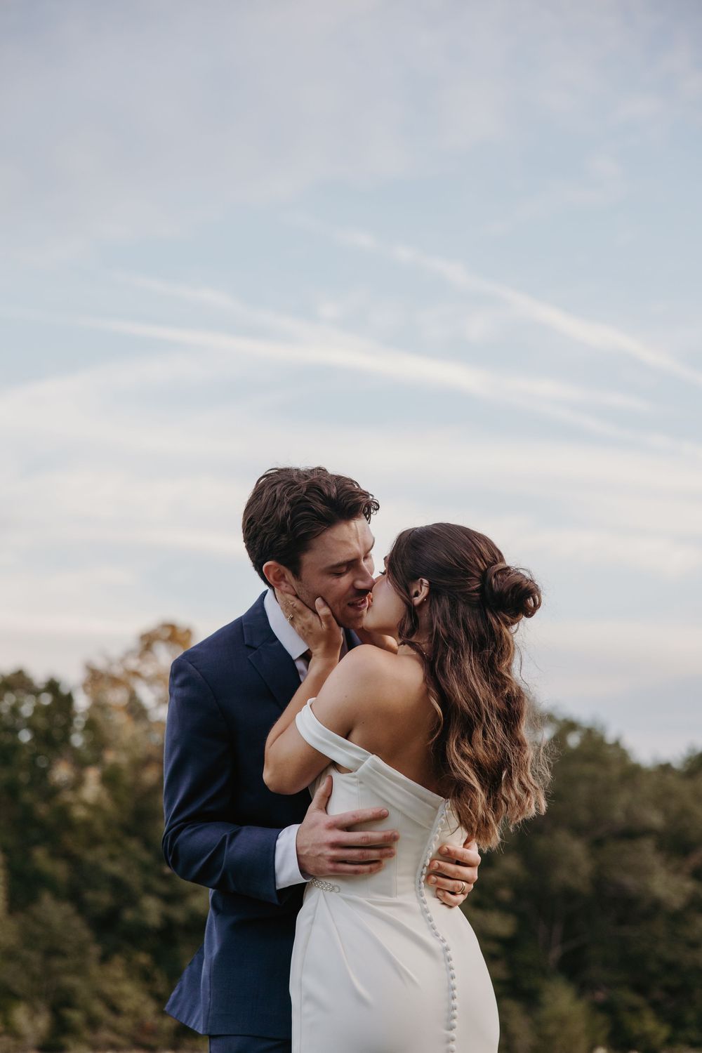 A romantic wedding moment captured against a soft blue sky during sunset.