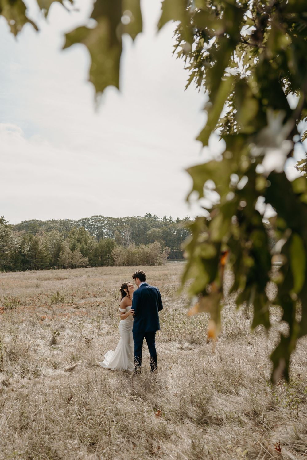 Newlyweds share an intimate moment in a golden meadow framed by tree branches.