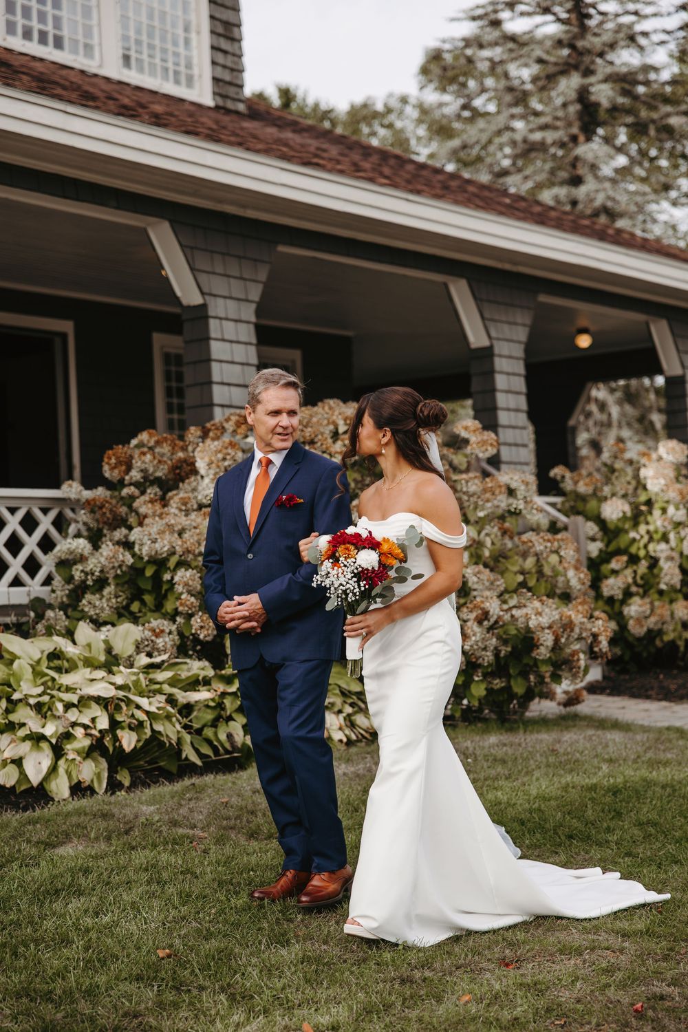 A wedding couple shares intimate moments on a lawn in front of a house with blooming flowers.