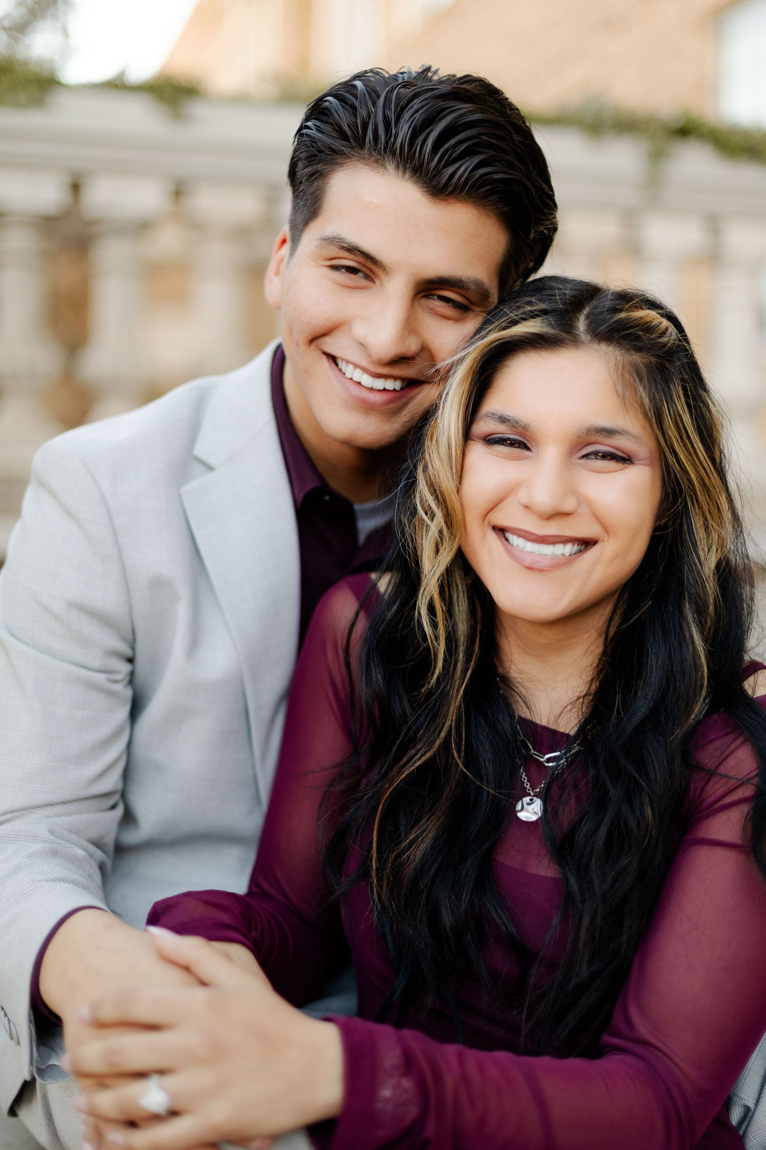 Stylish couple in burgundy and grey formal wear share an intimate moment outdoors.
