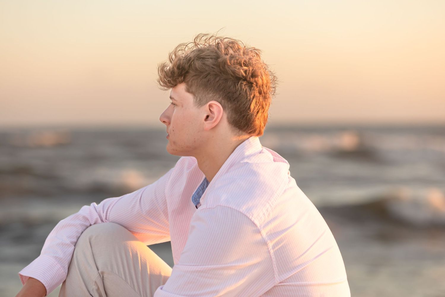 Sunset beach portrait of person in white shirt sitting on sand.