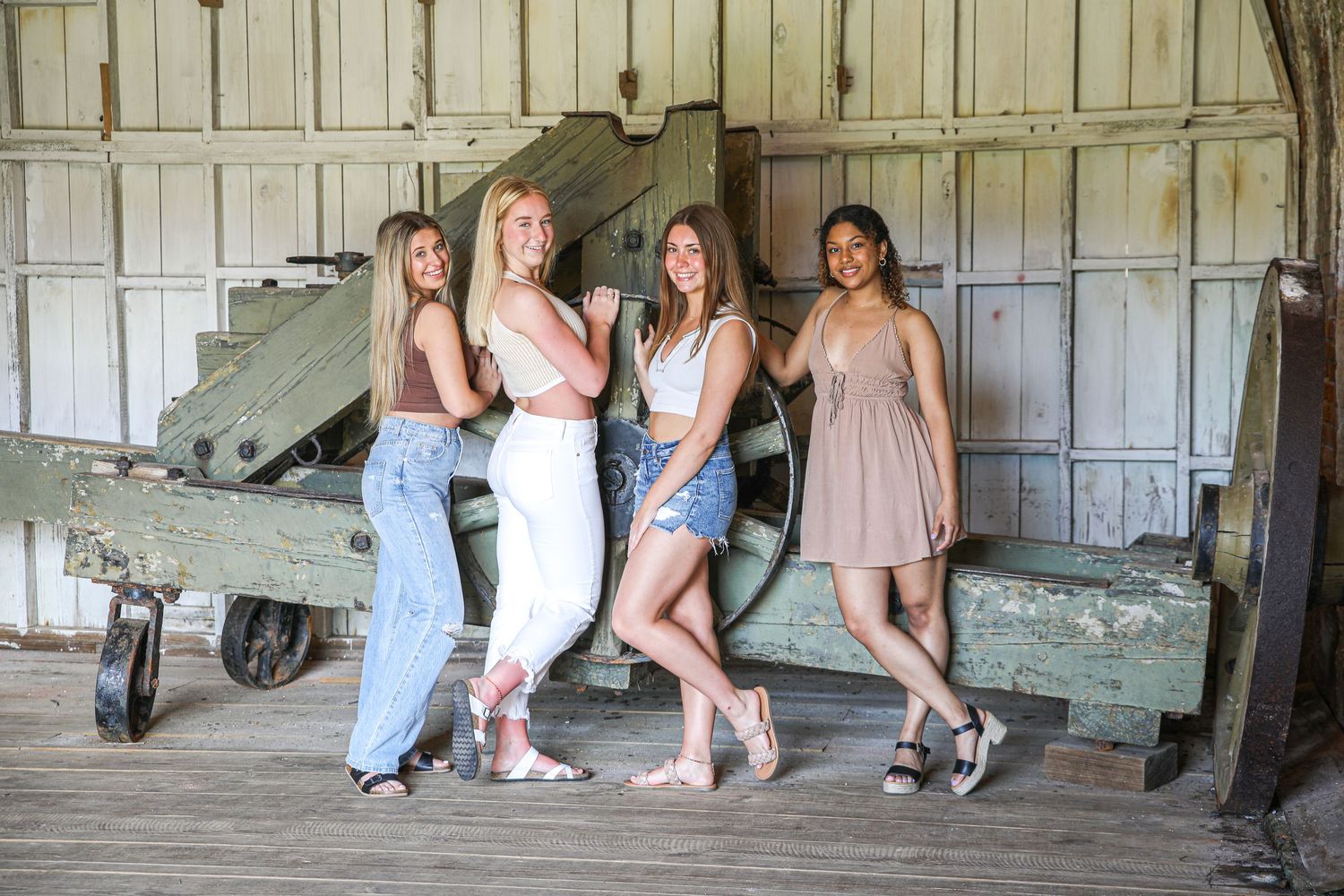 A group poses casually against a vintage military vehicle in a rustic barn setting.