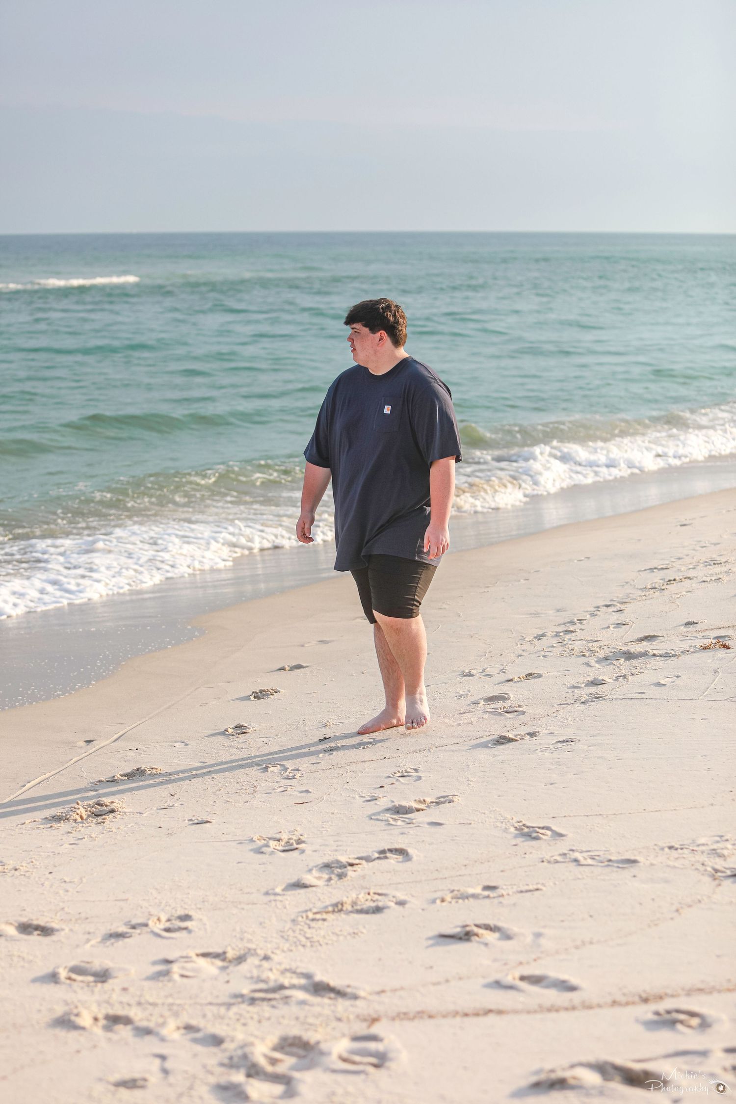 Person walking alone on sandy beach leaving footprints along ocean shoreline.