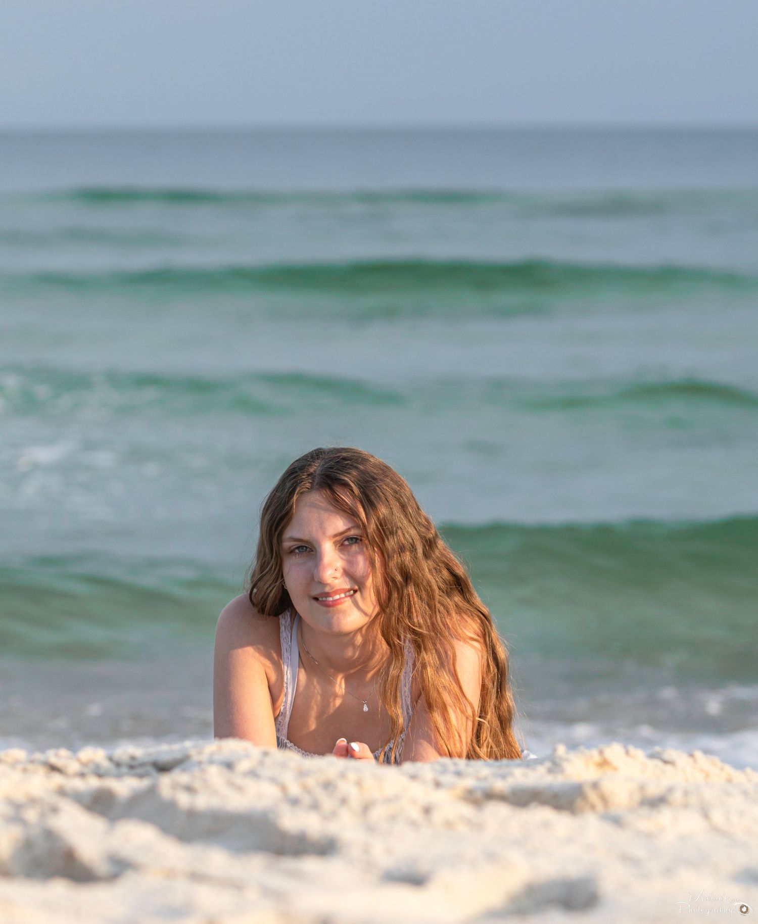 Beachside portrait of person lying in white sand with ocean waves in background.