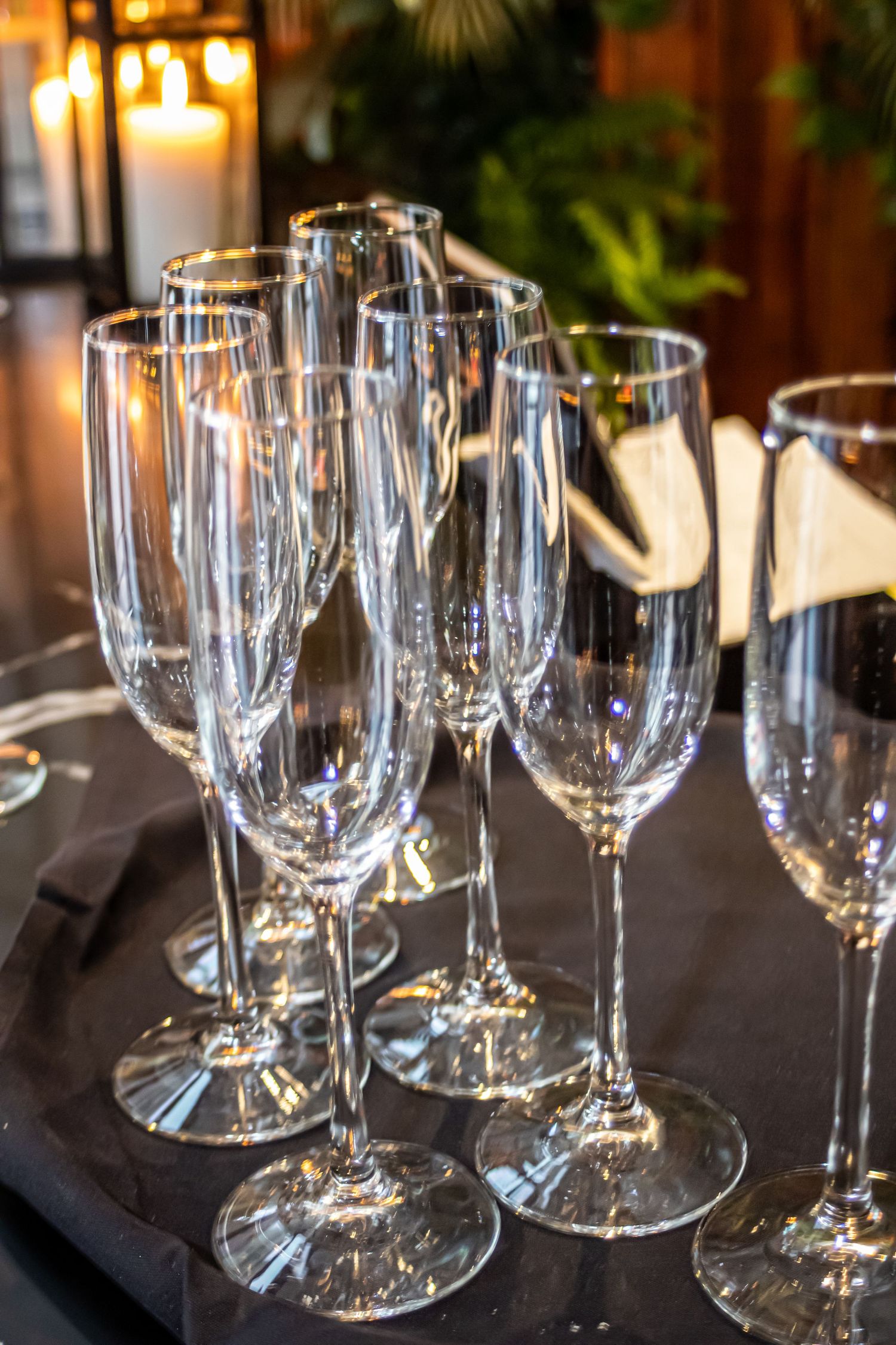 Empty champagne flutes arranged on dark table with ambient lighting and greenery in background.