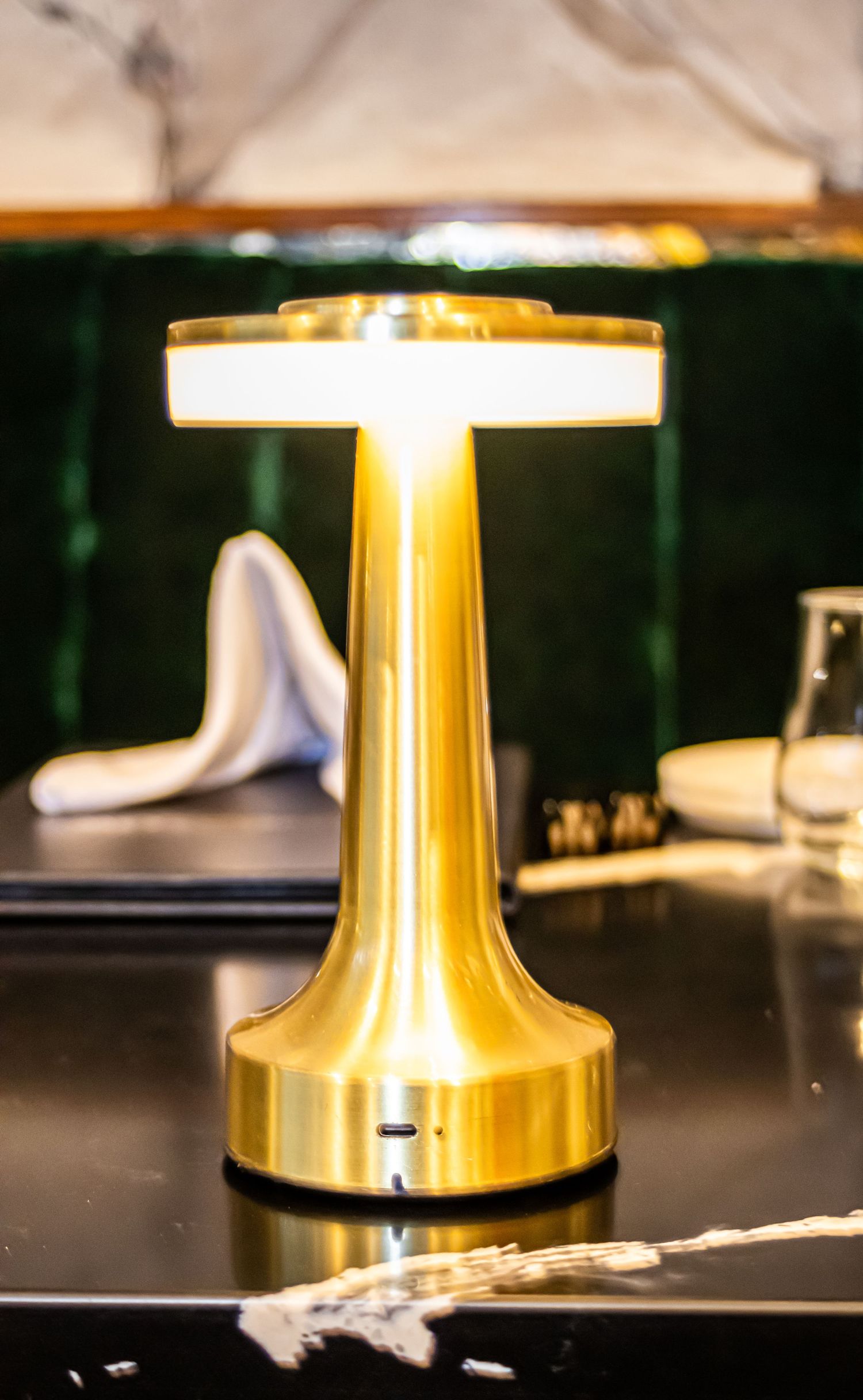 Modern gold table lamp with illuminated top on dark surface in luxurious setting.