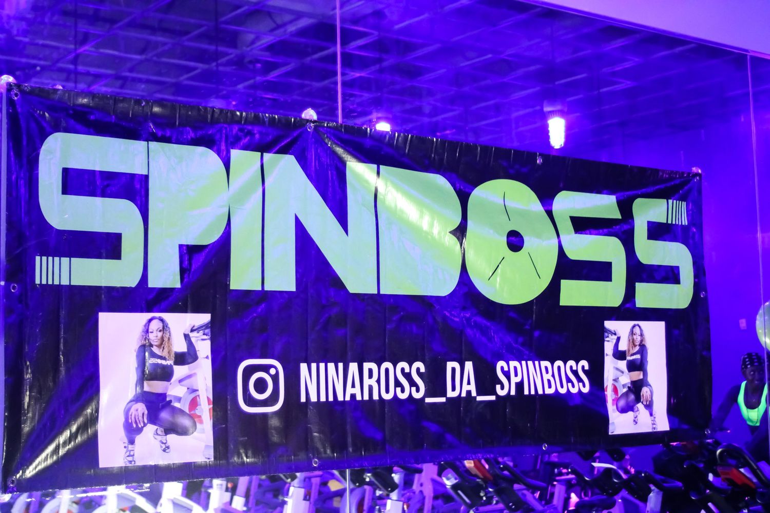 Illuminated SpinBoss sign with social media handle displayed in purple lighting at an event.
