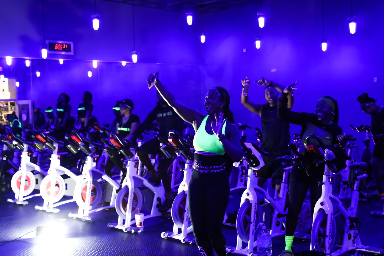 Group exercise class participants working out in a room lit with purple ambient lighting.