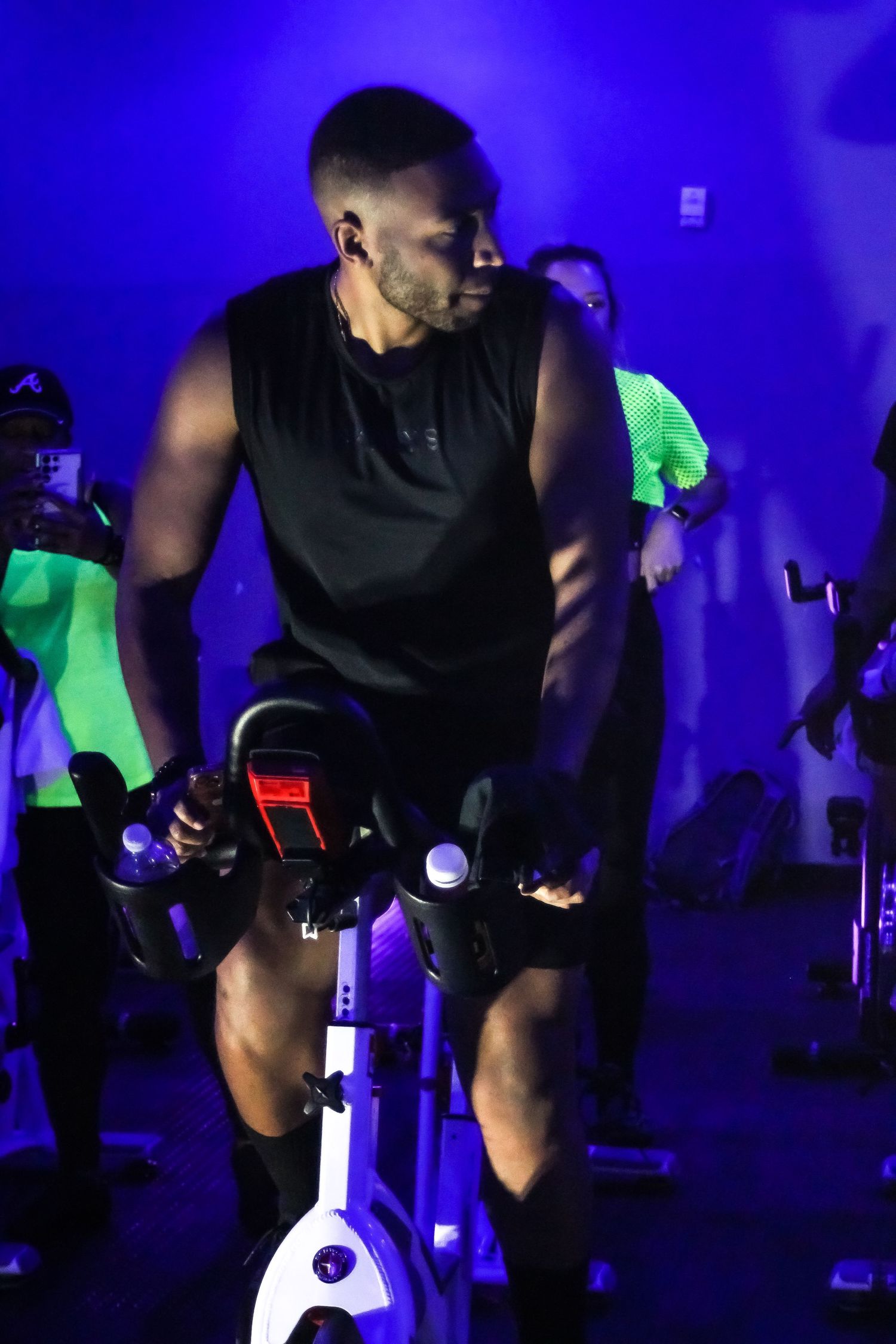 Fitness instructor leading an intense indoor cycling class in a dark room with blue lighting.