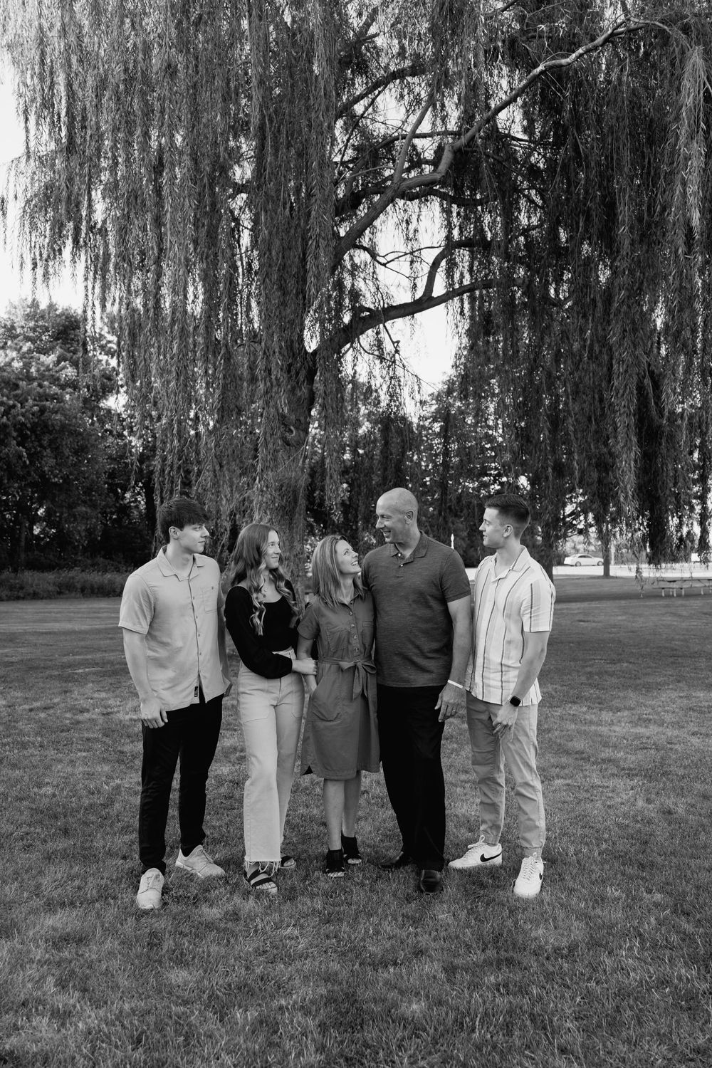 Group of people standing together under a weeping willow tree in a park setting.