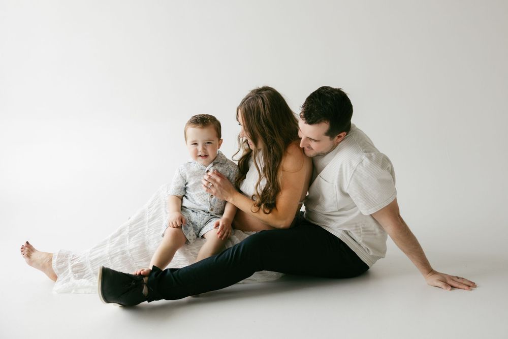 Family portrait in studio with parents and baby sitting together on white background.