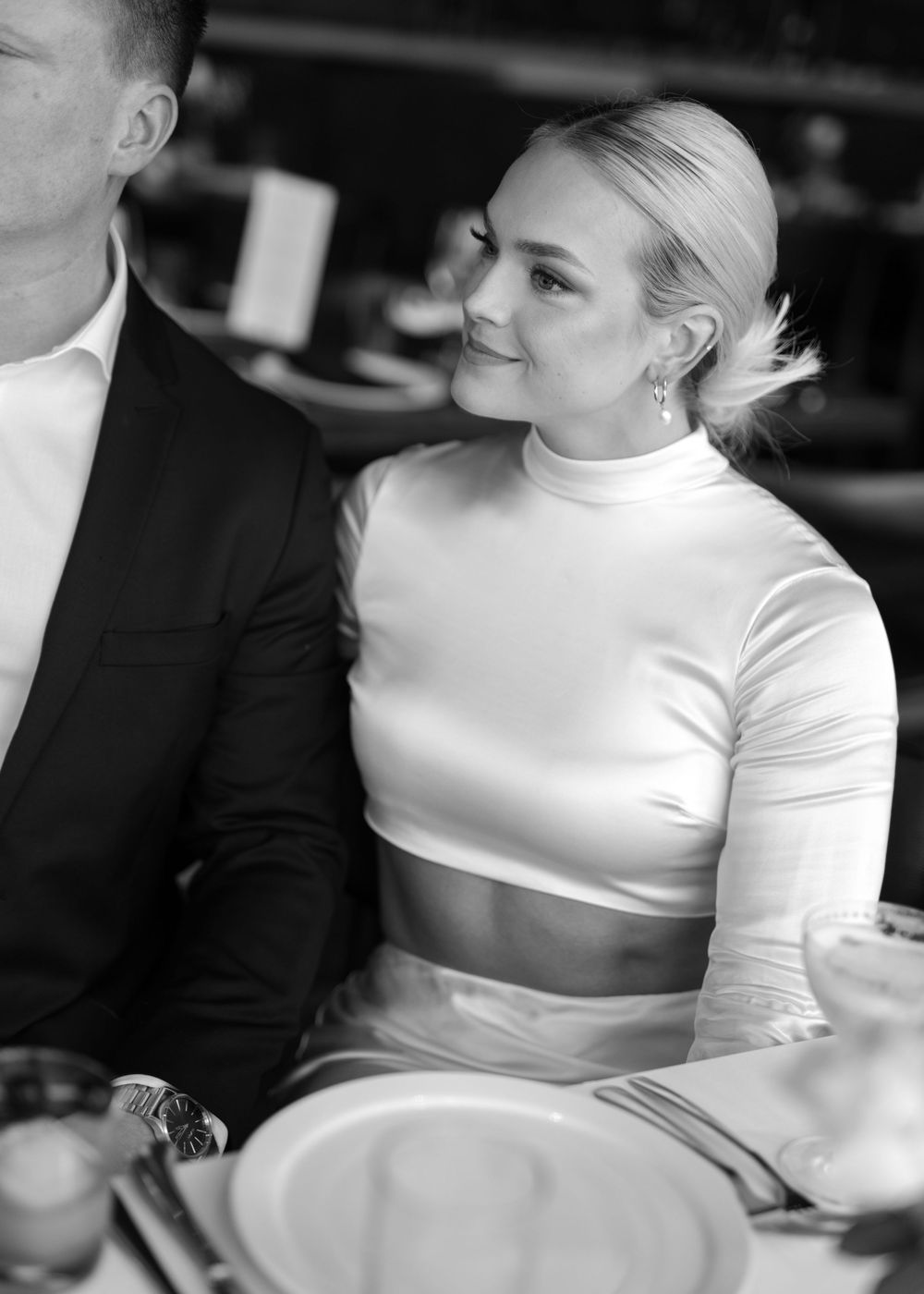 Woman in white crop top smiles during elegant dinner setting in black and white photograph.