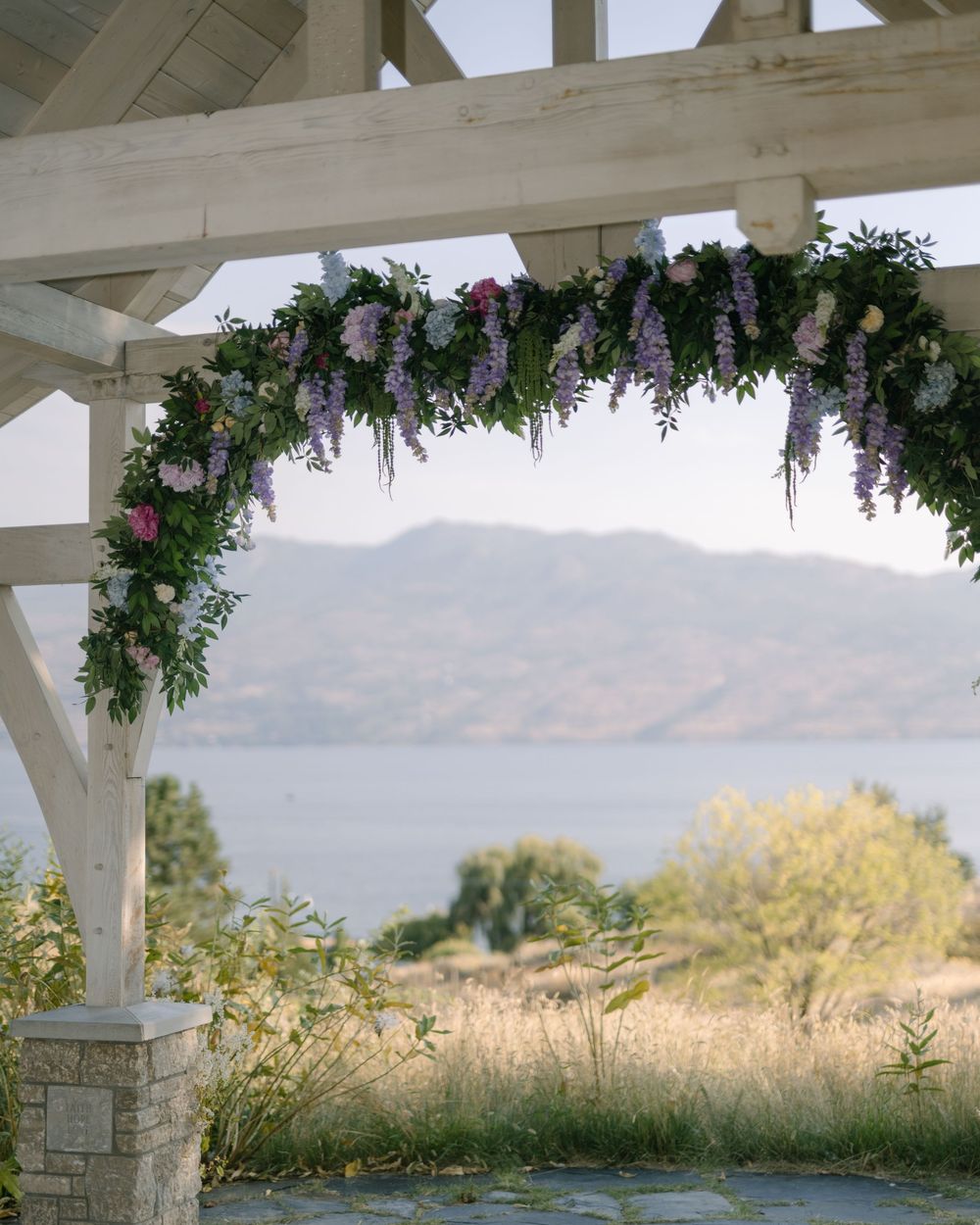 Wedding venue pergola decorated with floral arrangements against mountain backdrop.