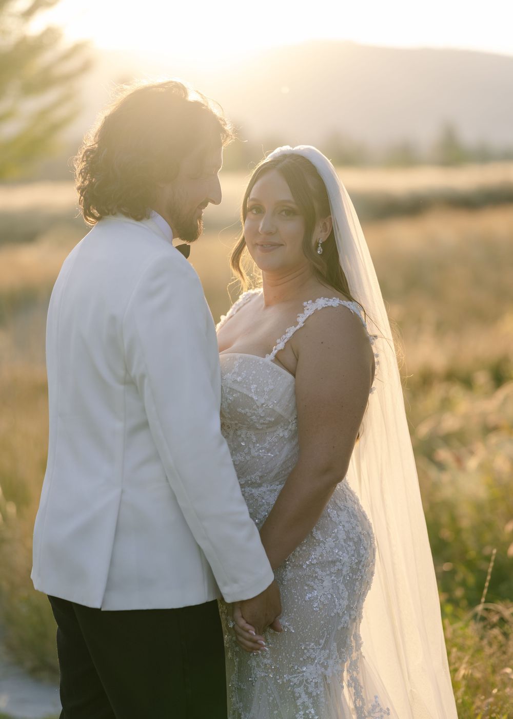 Intimate sunset portrait of bride and groom sharing romantic moment in field.