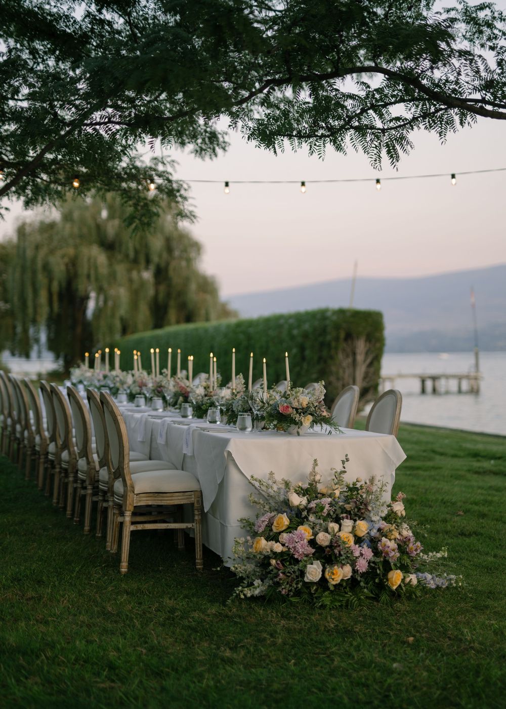 Elegant outdoor wedding reception setup with long tables and floral arrangements by the lake.