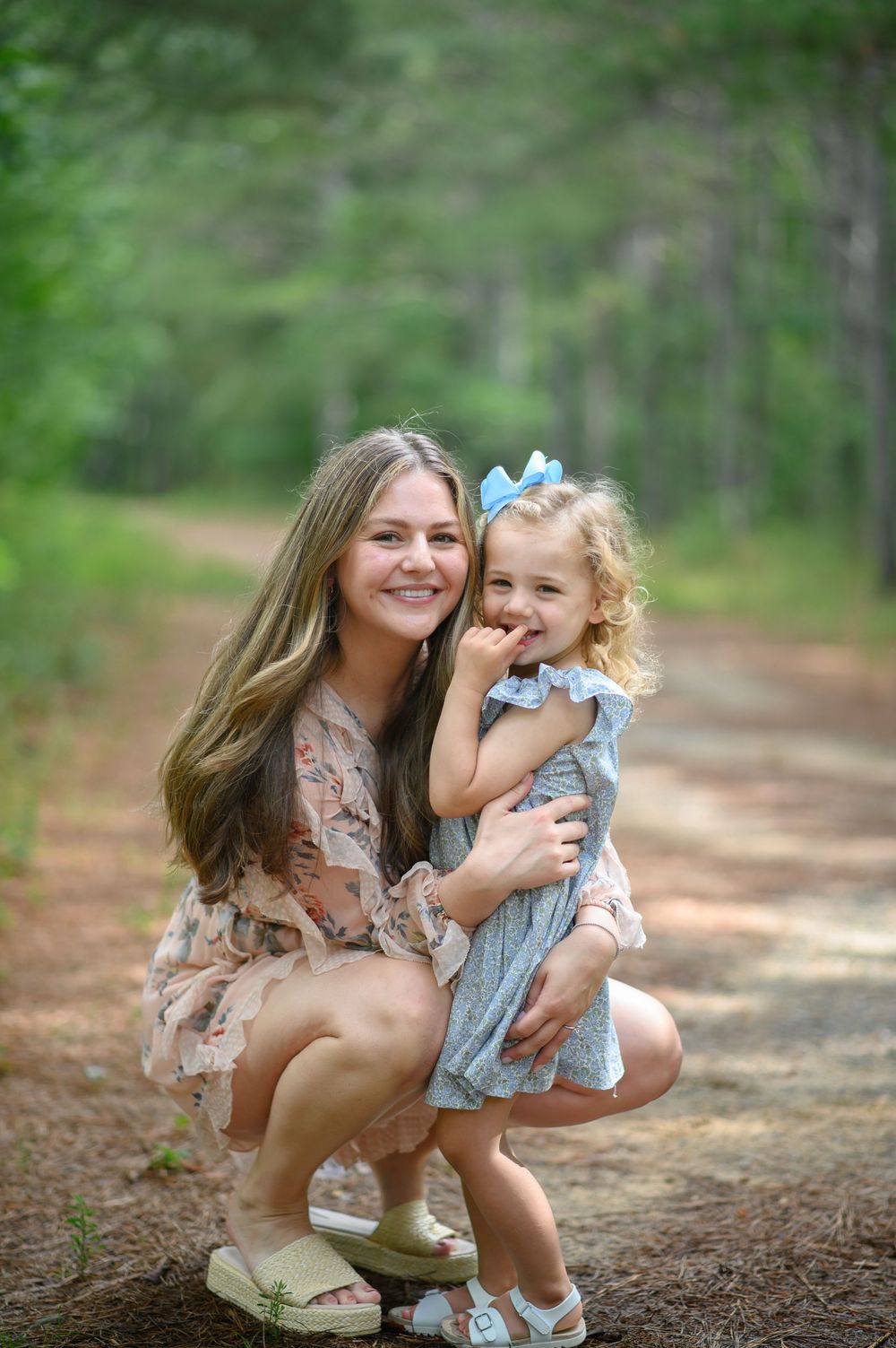 A loving family moment captured outdoors on a sunlit forest path with natural greenery in the background.