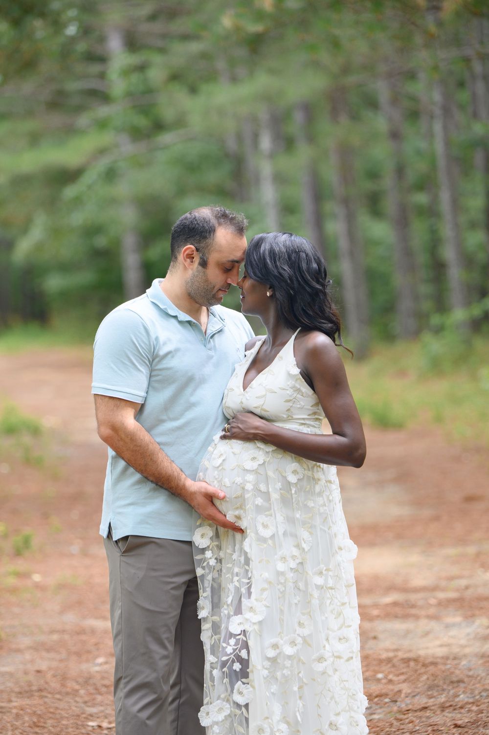 A loving couple shares a romantic moment on a forest trail while wearing white and grey casual attire.