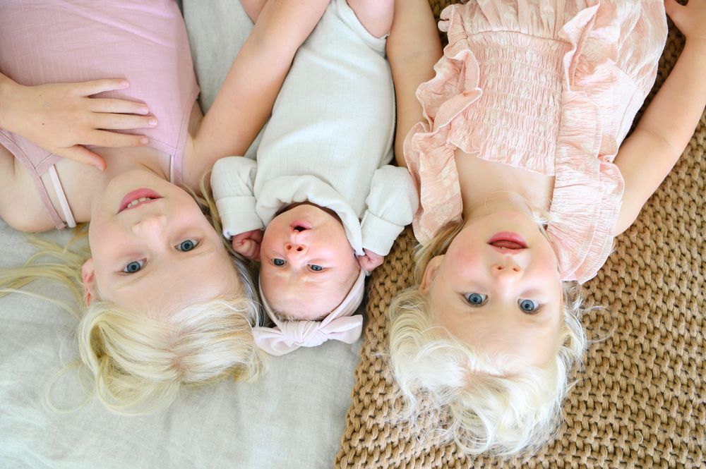 Baby lying on tan carpet wearing a peach dress smiles while looking at camera from above. family photos in canton, ga