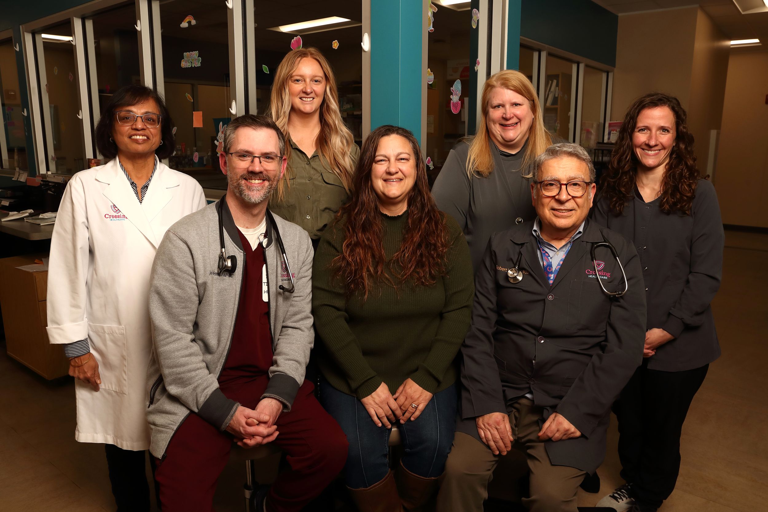 A group of diverse healthcare professionals pose together in a medical facility hallway.