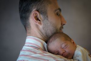 A father tenderly holds his sleeping newborn baby against his shoulder in a heartwarming close-up portrait.