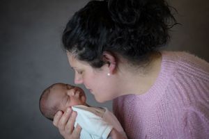 A mother tenderly nuzzles her newborn baby wrapped in white, sharing an intimate bonding moment.