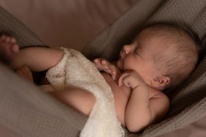 Peaceful newborn baby sleeping curled up on a soft blanket in warm, natural light.