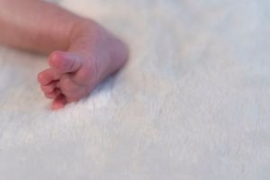 Close-up of a newborn baby's tiny hand resting gently on a soft white blanket.