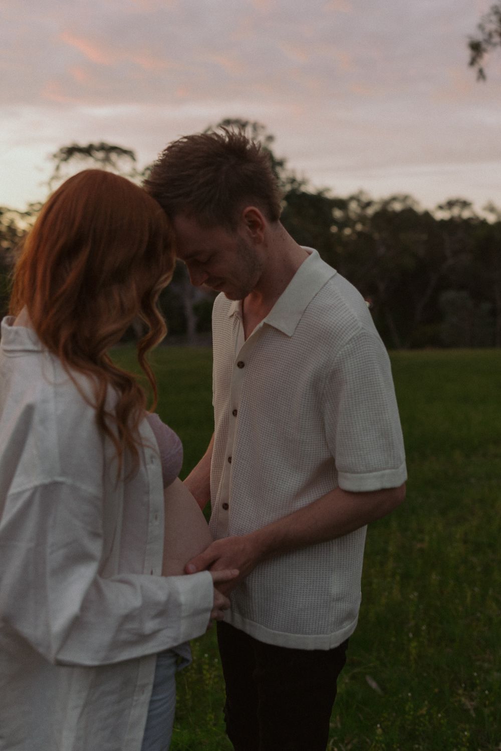 A couple shares intimate moments in a green field during sunset.