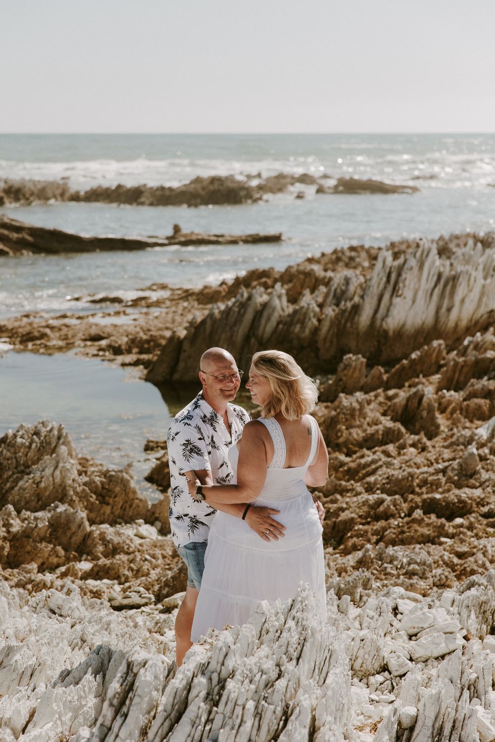 A romantic couple poses on dramatic rocky cliffs overlooking the ocean waves.