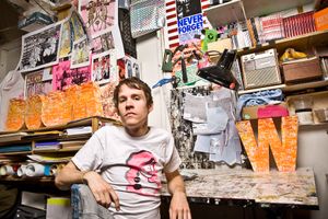 Young male artist relaxing in colorful creative studio surrounded by artwork and supplies.