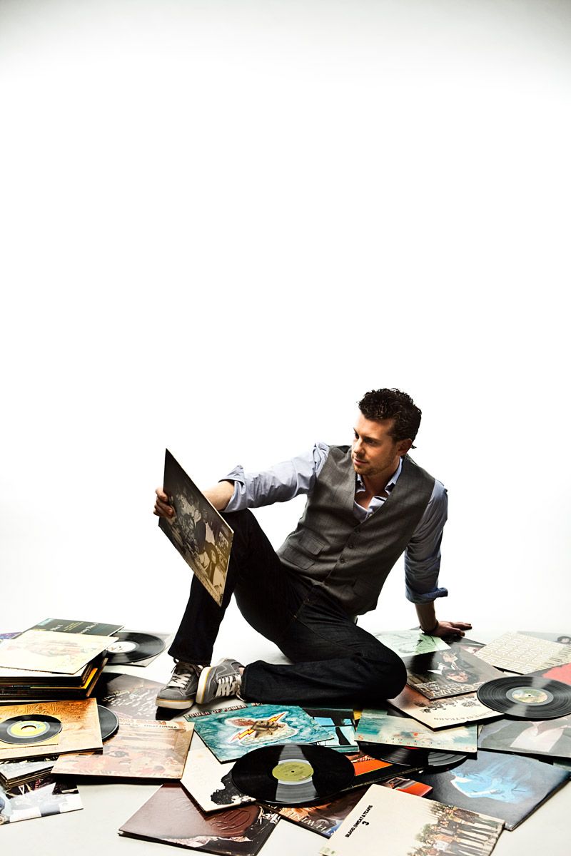 Young man sitting on floor surrounded by scattered vinyl record albums.
