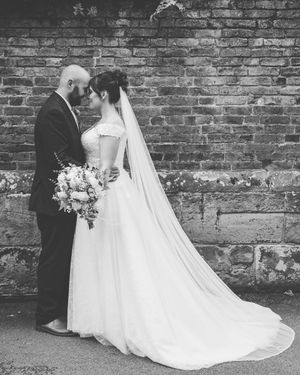 Black and white photo of a bride and groom sharing an intimate moment against a rustic brick wall.