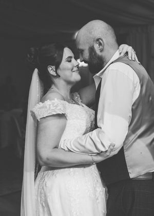 Black and white photo of a bride and groom sharing an intimate moment, smiling closely during their first dance.