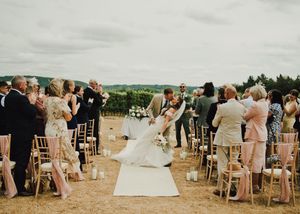 Bride and groom share a romantic dip kiss at outdoor vineyard wedding ceremony with guests applauding.