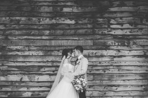 A romantic black and white wedding photo of a couple embracing in front of a rustic wooden wall.