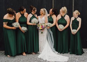 A row of bridesmaids in emerald green dresses stand alongside a bride in white, holding coordinated white bouquets.