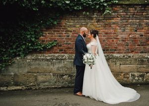 Bride and groom share a romantic moment against a rustic brick wall adorned with ivy, bride holding a white bouquet.
