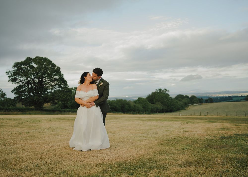 Bride and groom share a romantic moment in a lush green countryside field on their wedding day.