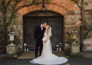 Bride and groom share a romantic kiss in front of rustic wooden doors at an elegant brick wedding venue.