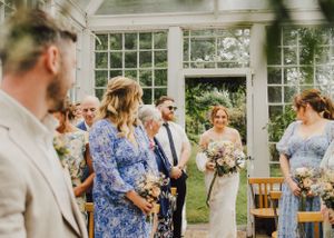 Wedding party gathered in a bright conservatory with bridesmaids in blue dresses.