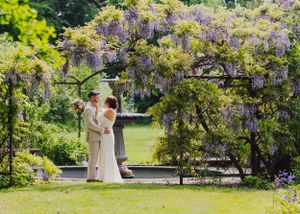 Couple sharing intimate moment under blooming wisteria in garden setting.
