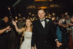 Bride and groom exit wedding reception through sparkler tunnel, smiling joyfully at night.