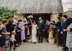 Wedding guests throw confetti over newlyweds as they exit a rustic barn on their special day.