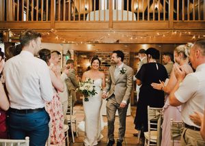 Bride and groom walk down the aisle in a rustic barn wedding venue with fairy lights and applauding guests.