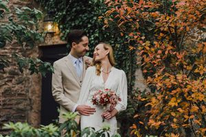 A couple shares a romantic moment in a garden with vibrant orange autumn foliage and stone walls in the background.